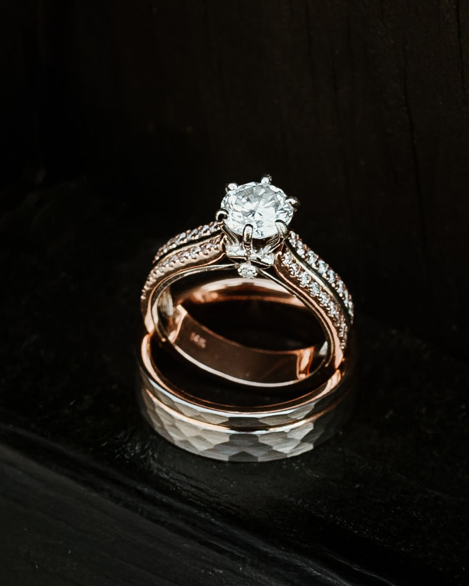 Rose gold wedding bands and engagement ring photographed on dark surface with dramatic lighting.