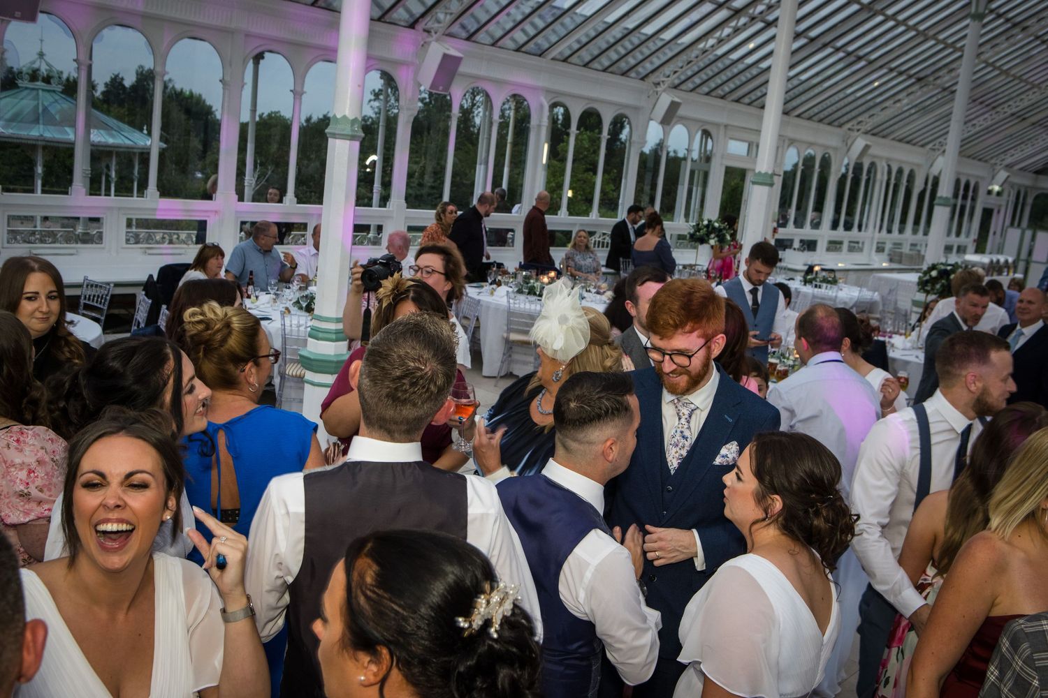 Lively wedding reception with guests dancing under glass ceiling.