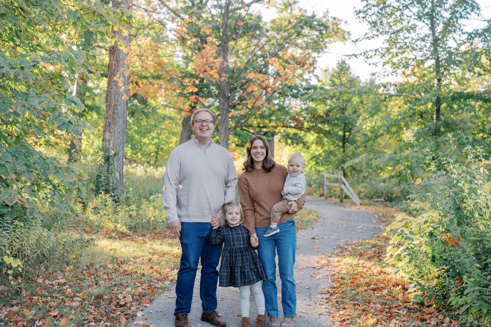 Family photo session on a tree-lined path with golden autumn leaves.