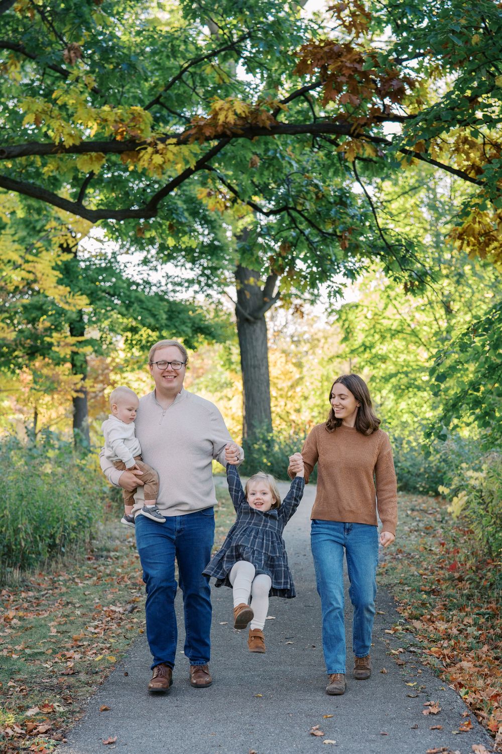 Family walking together on autumn path with colorful trees overhead.