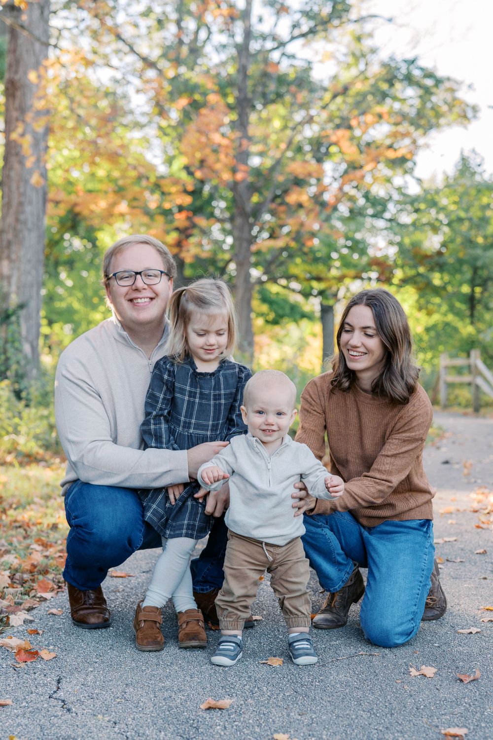 Casual family portrait session on a gravel path with fall colors in the background.