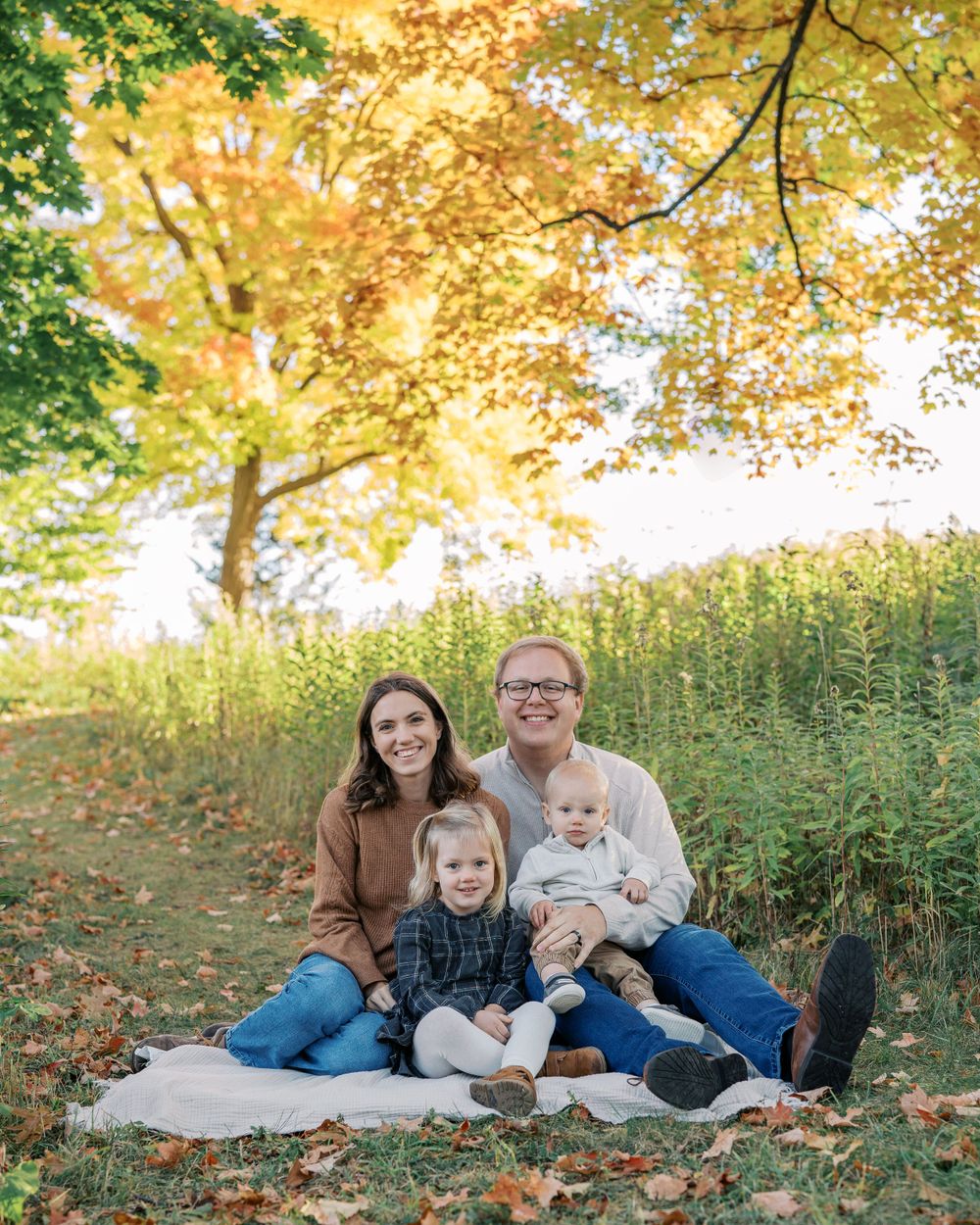 Family photo session in a park with golden autumn leaves and natural lighting.