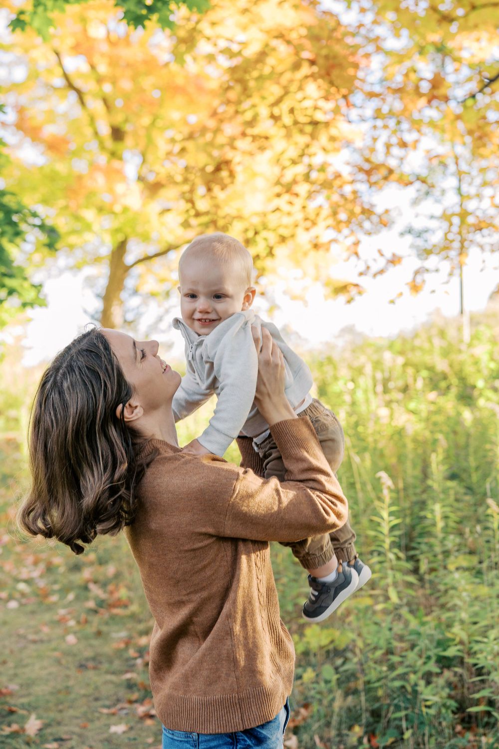 Joyful moment between parent and baby against autumn trees with golden leaves.