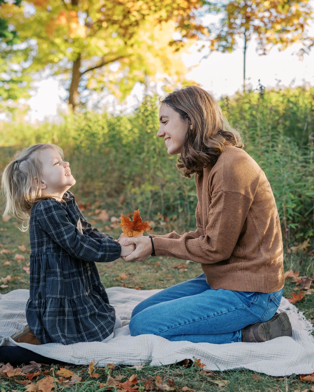 Heartwarming autumn scene of sharing fallen leaf on picnic blanket outdoors.