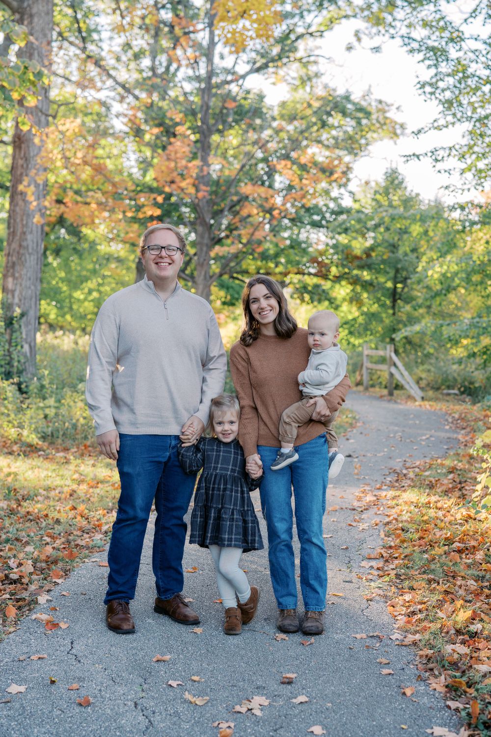 Family portrait session on a gravel path surrounded by fall foliage.