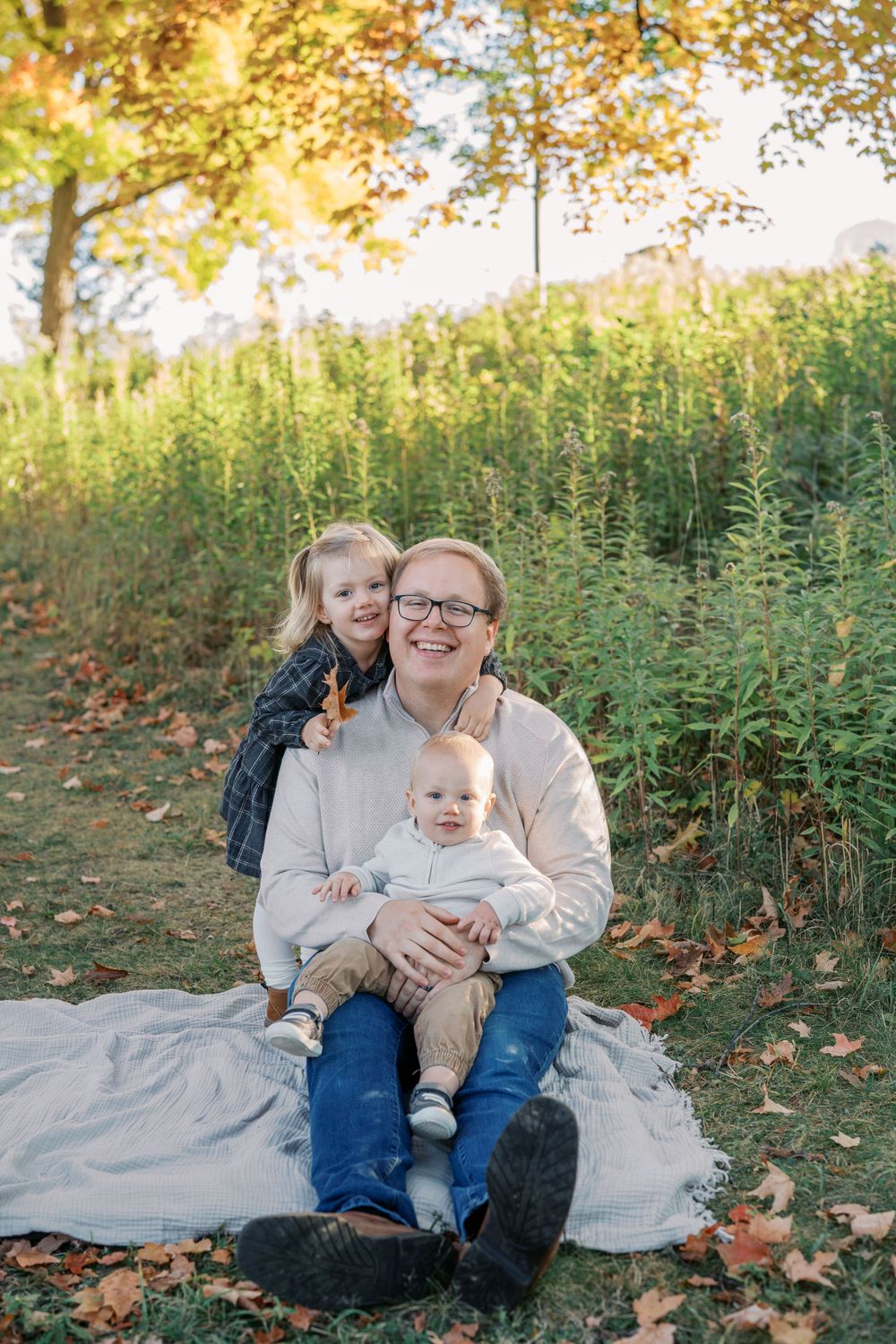 Family portrait on blanket with autumn foliage and tall grass in background.