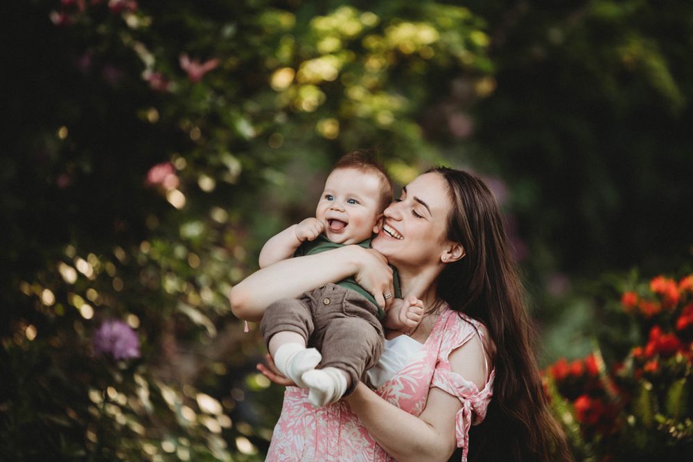 A joyful moment shared between parent and baby in a garden with colorful flowers and natural bokeh lighting.