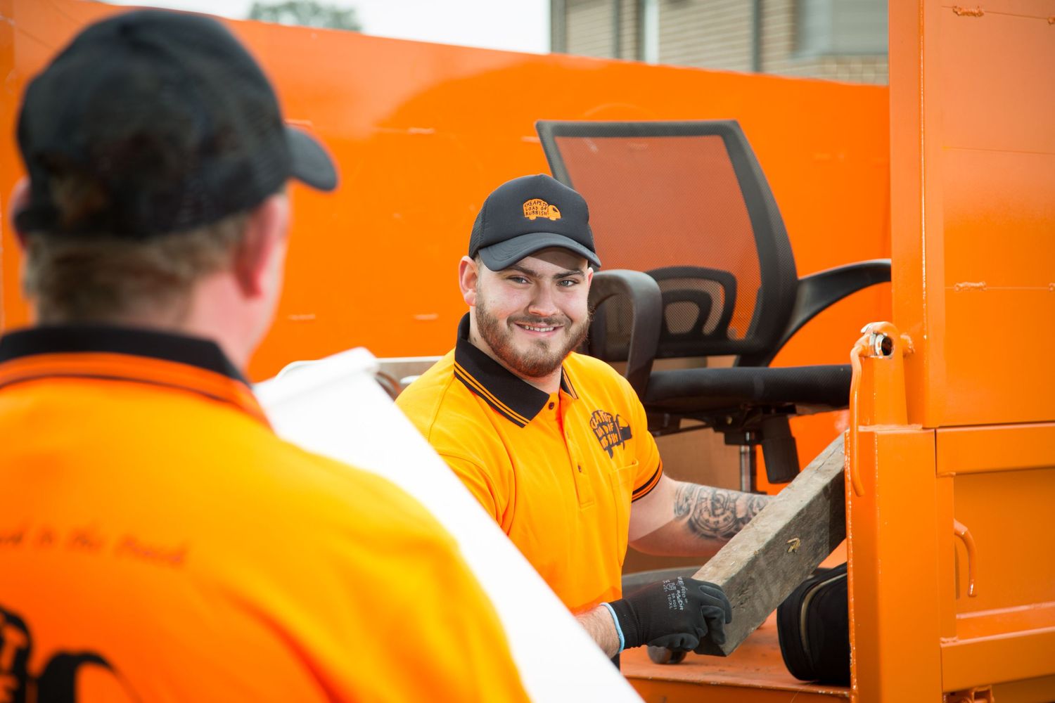Workers in high-visibility orange uniforms reviewing paperwork near delivery vehicle.