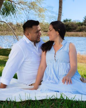 Couple sits close together on a blanket by a lake, gazing lovingly at each other.