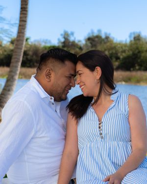 Couple leans in close together outdoors by a lake, smiling warmly at each other.