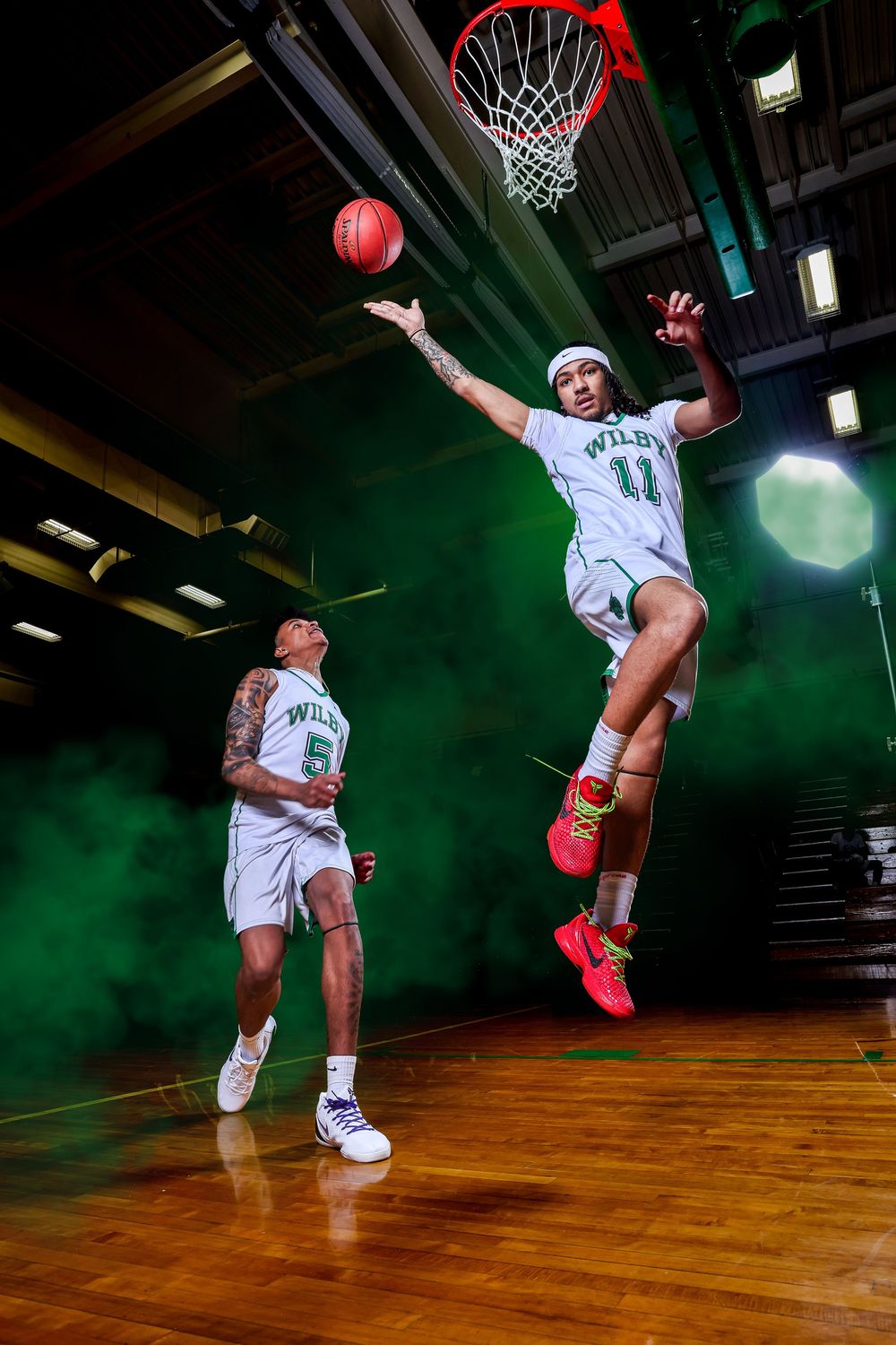 Basketball player in white jersey and red shoes performs dynamic slam dunk sequence on indoor court with green lighting.
