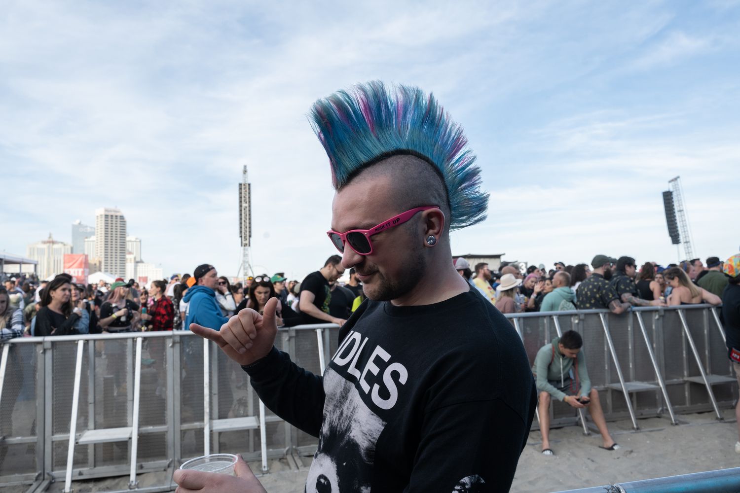 A man with a vibrant mohawk and stylish sunglasses enjoying the lively atmosphere at a music festival.