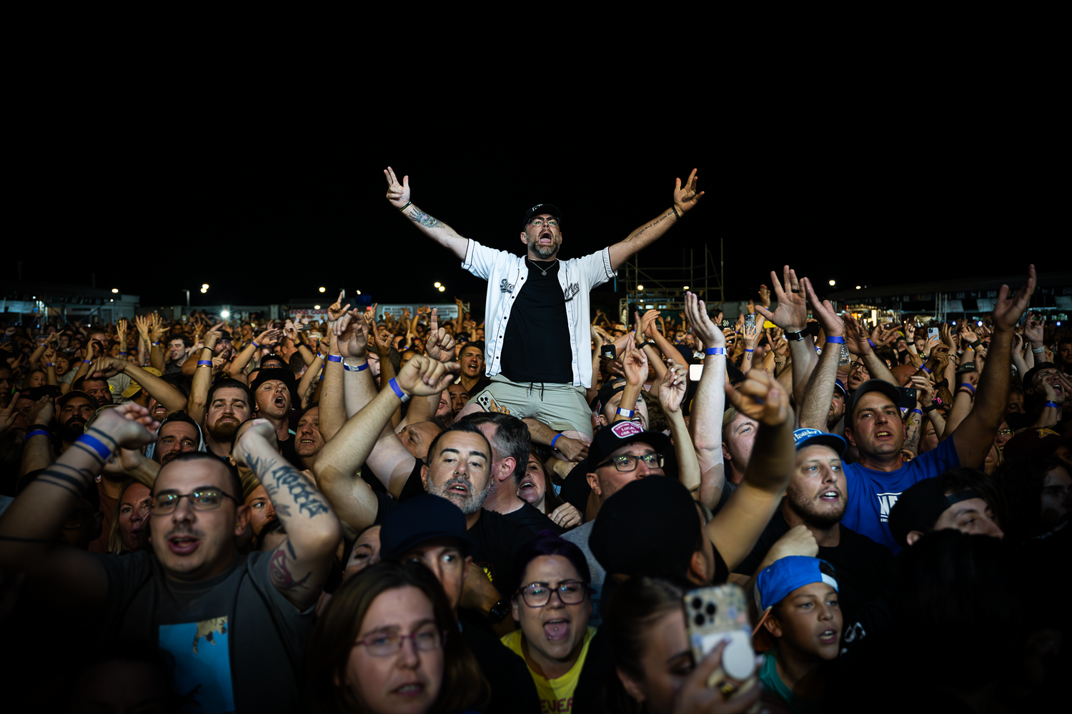 A man in a crowd raises his hands in the air, expressing excitement or celebration amidst the gathered people.