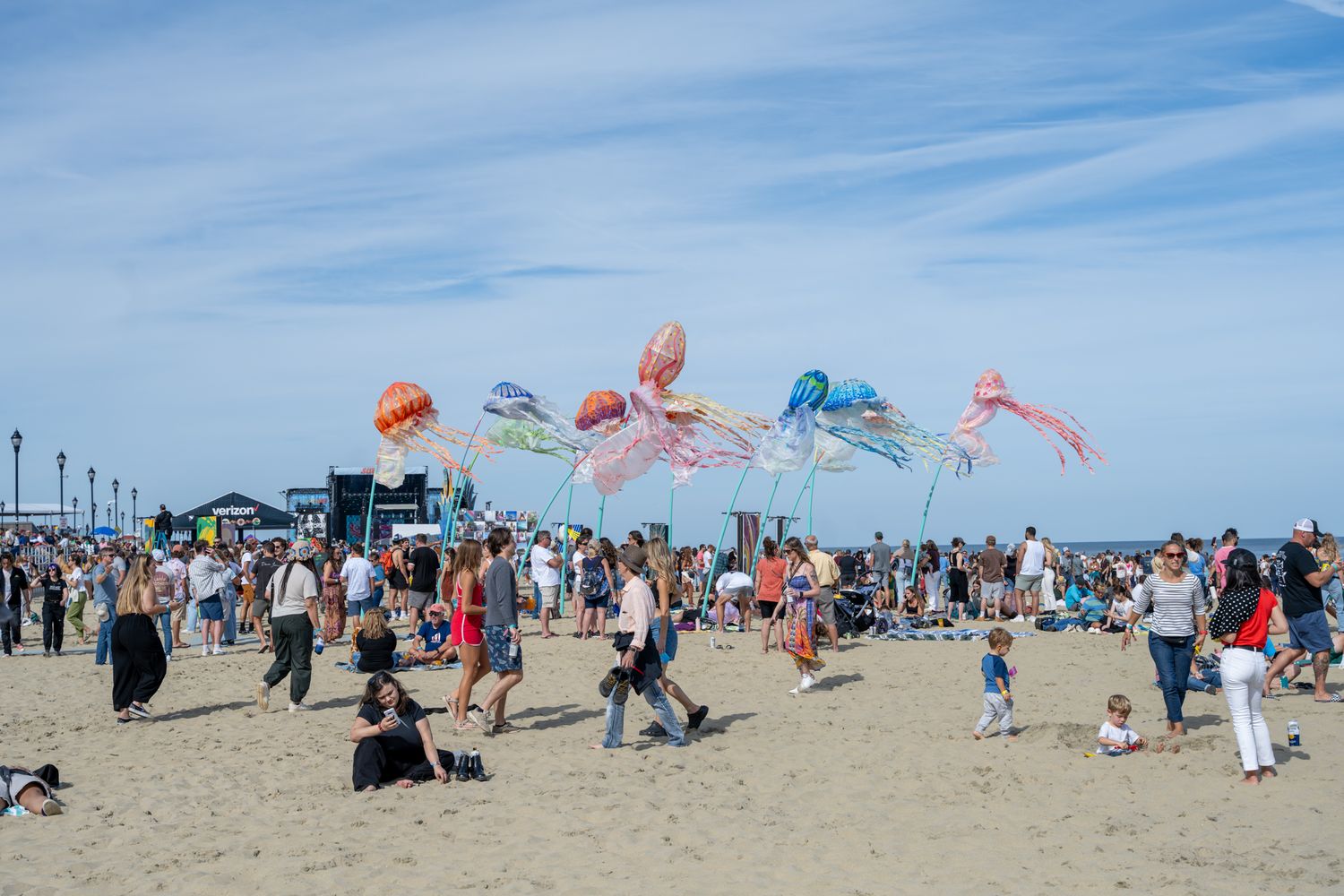 A lively beach scene filled with a crowd of people flying colorful kites against a clear blue sky.