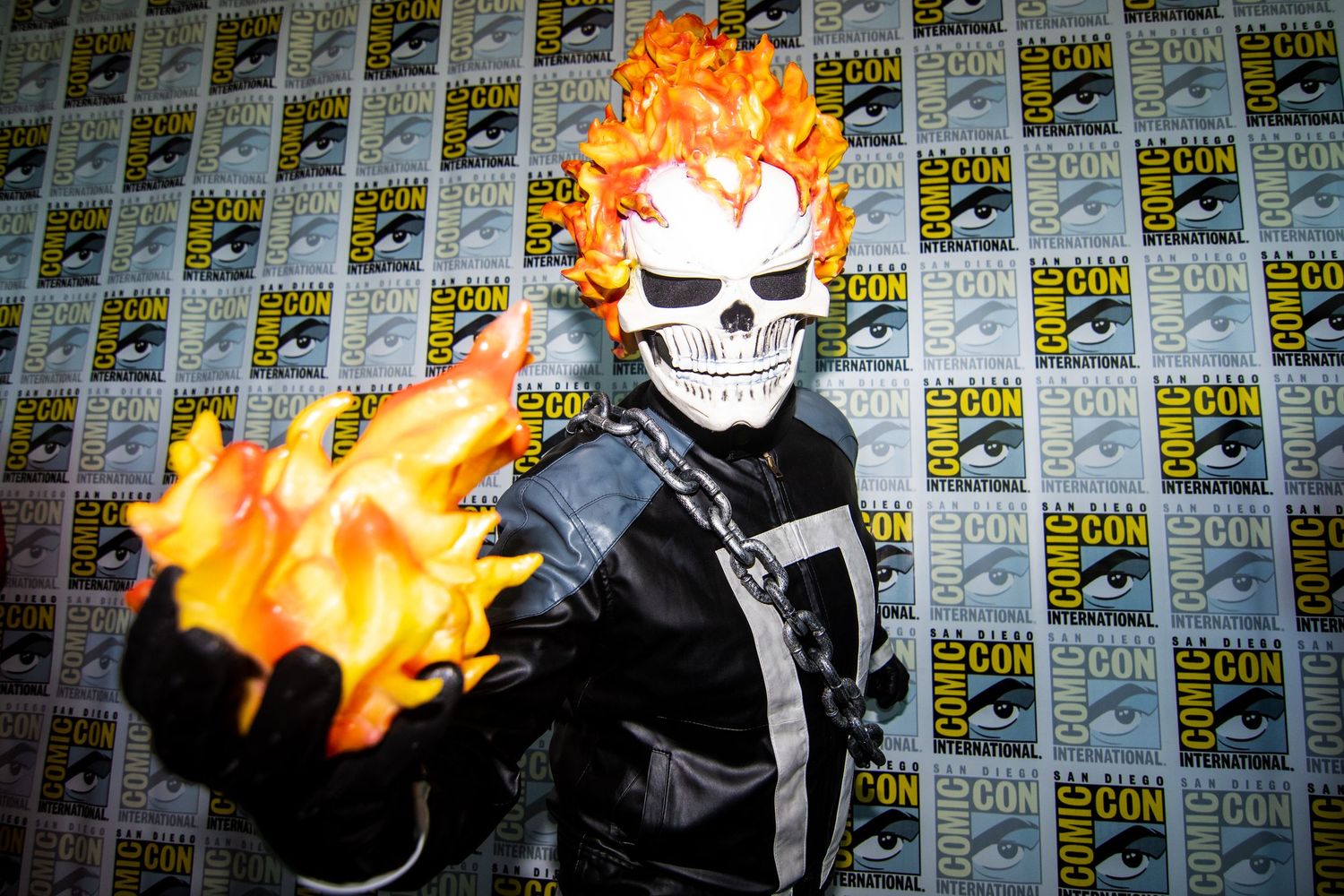 A man in a Ghost Rider costume holds a flickering flame, creating a striking contrast against the dark background.
