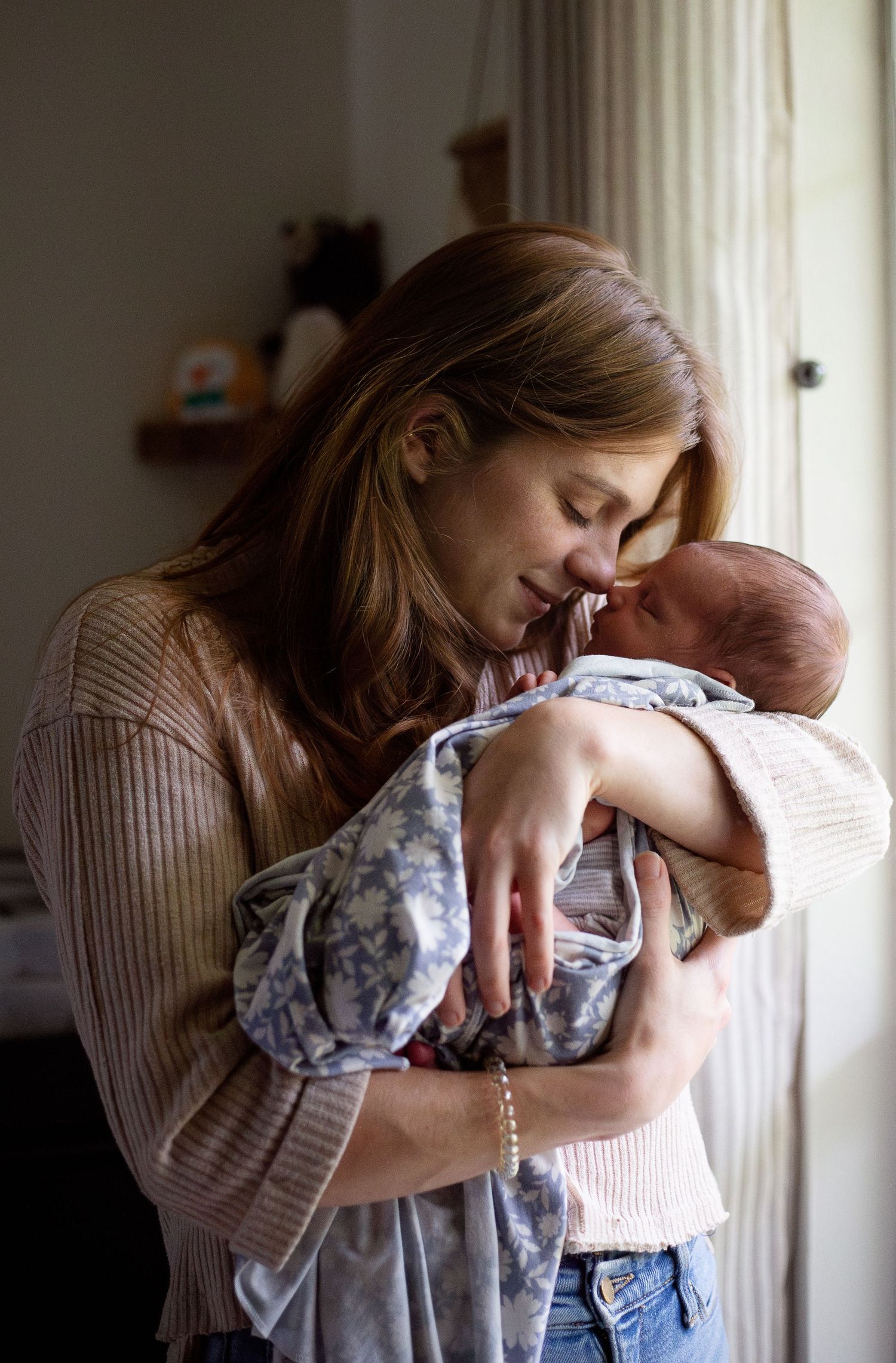 A tender moment between parent and newborn baby in soft natural window light.