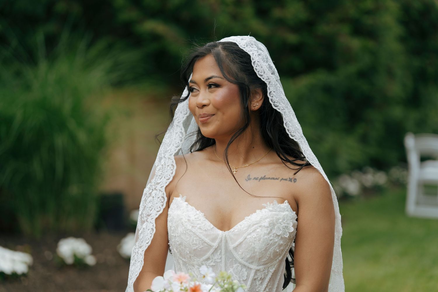 Beautiful bride in lace wedding dress and veil holding bouquet outdoors on her wedding day.