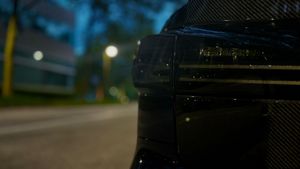 Close-up of a wet black carbon fiber spoiler with badge under street lights at night.