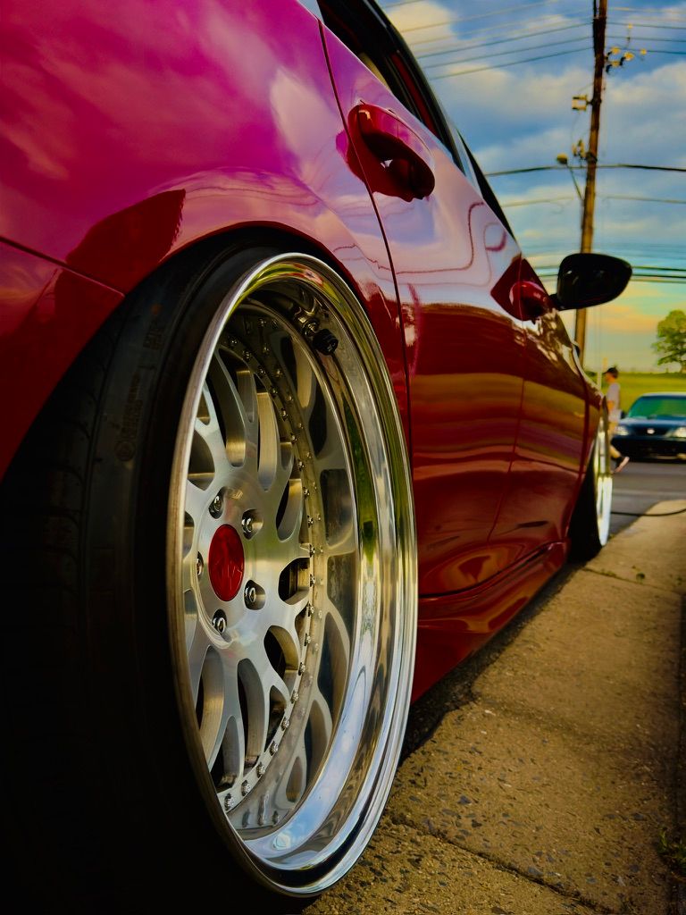 Slammed pink car with deep-dish polished BBS-style wheels at golden hour.