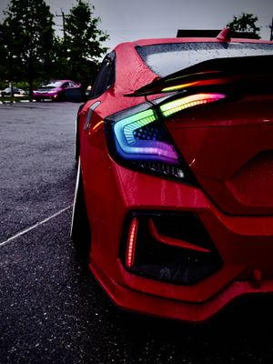 Red Honda Civic with RGB rainbow LED tail lights gleaming in a wet parking lot.