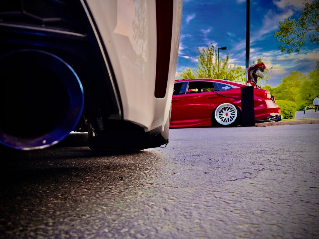 Low ground-level view of two modified cars with titanium exhaust tip under blue sky.