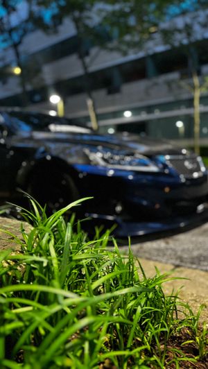 Black Lexus sedan parked near green grass under bright parking lot lights at night.