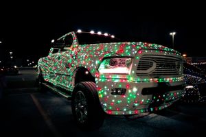 A pickup truck decorated with red and green Christmas lights parked in a lot at night.