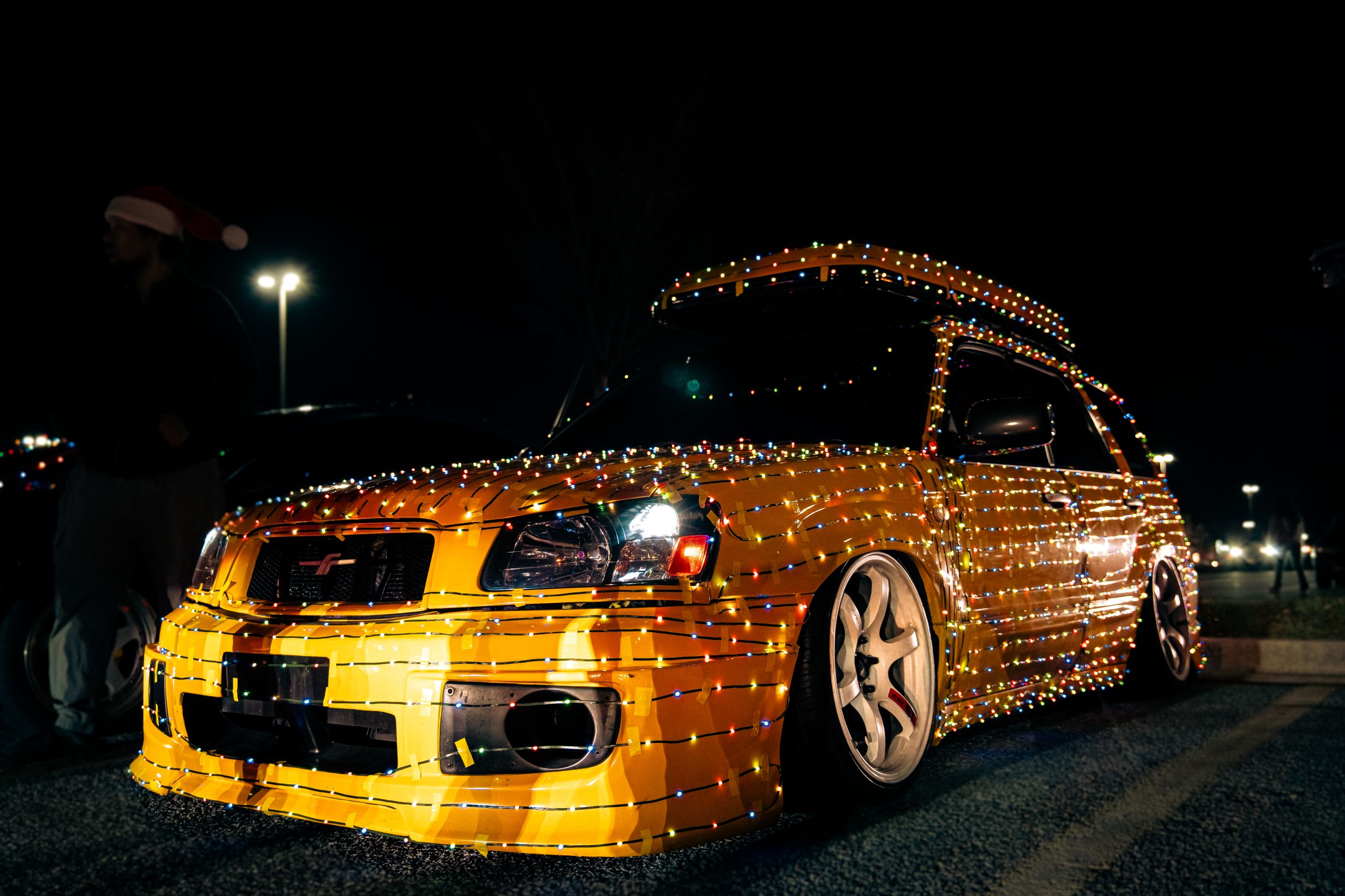 A lowered car fully covered in golden yellow Christmas lights parked at night.