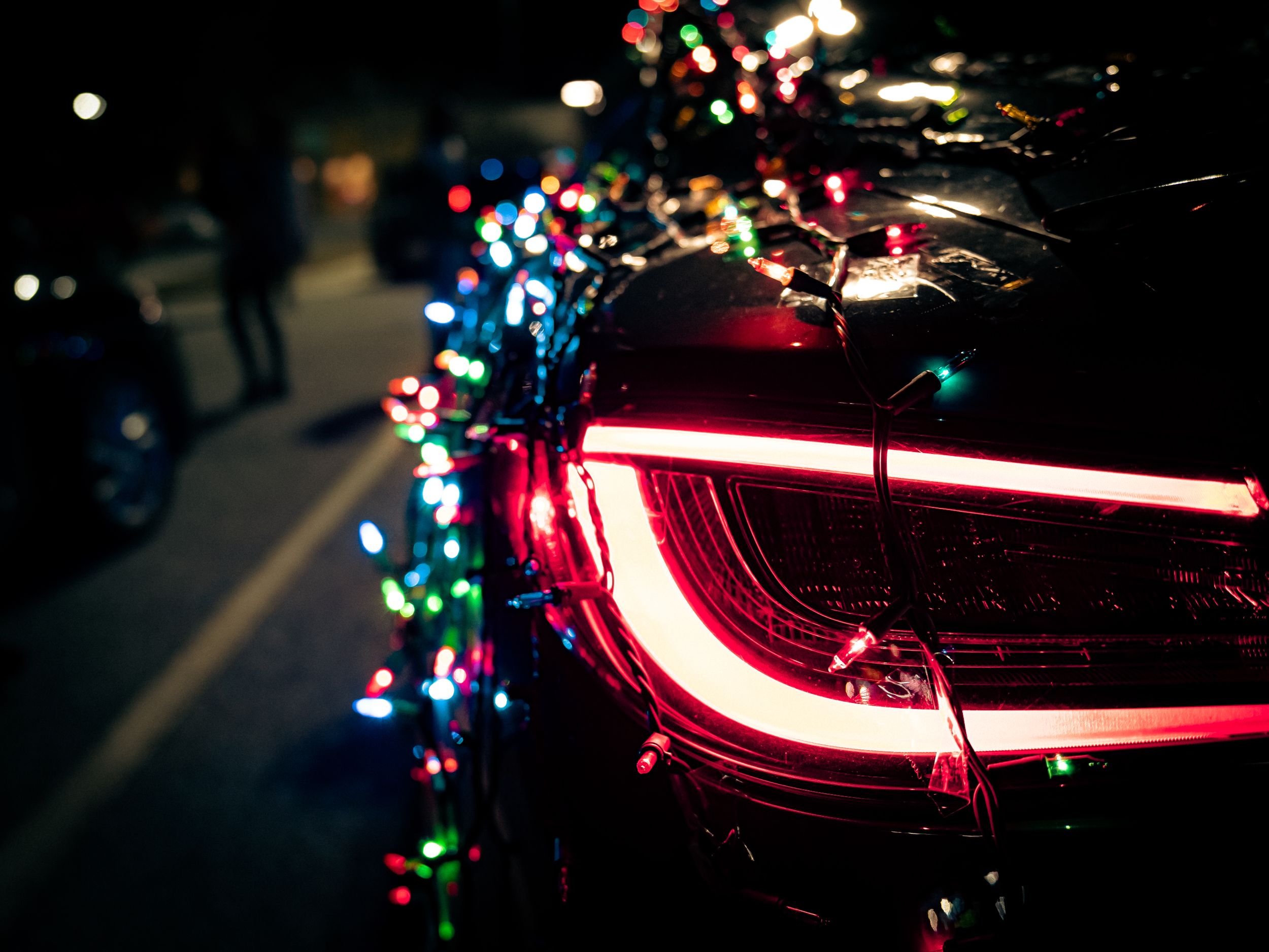 Close-up of a car tail light surrounded by colorful bokeh Christmas lights at night.