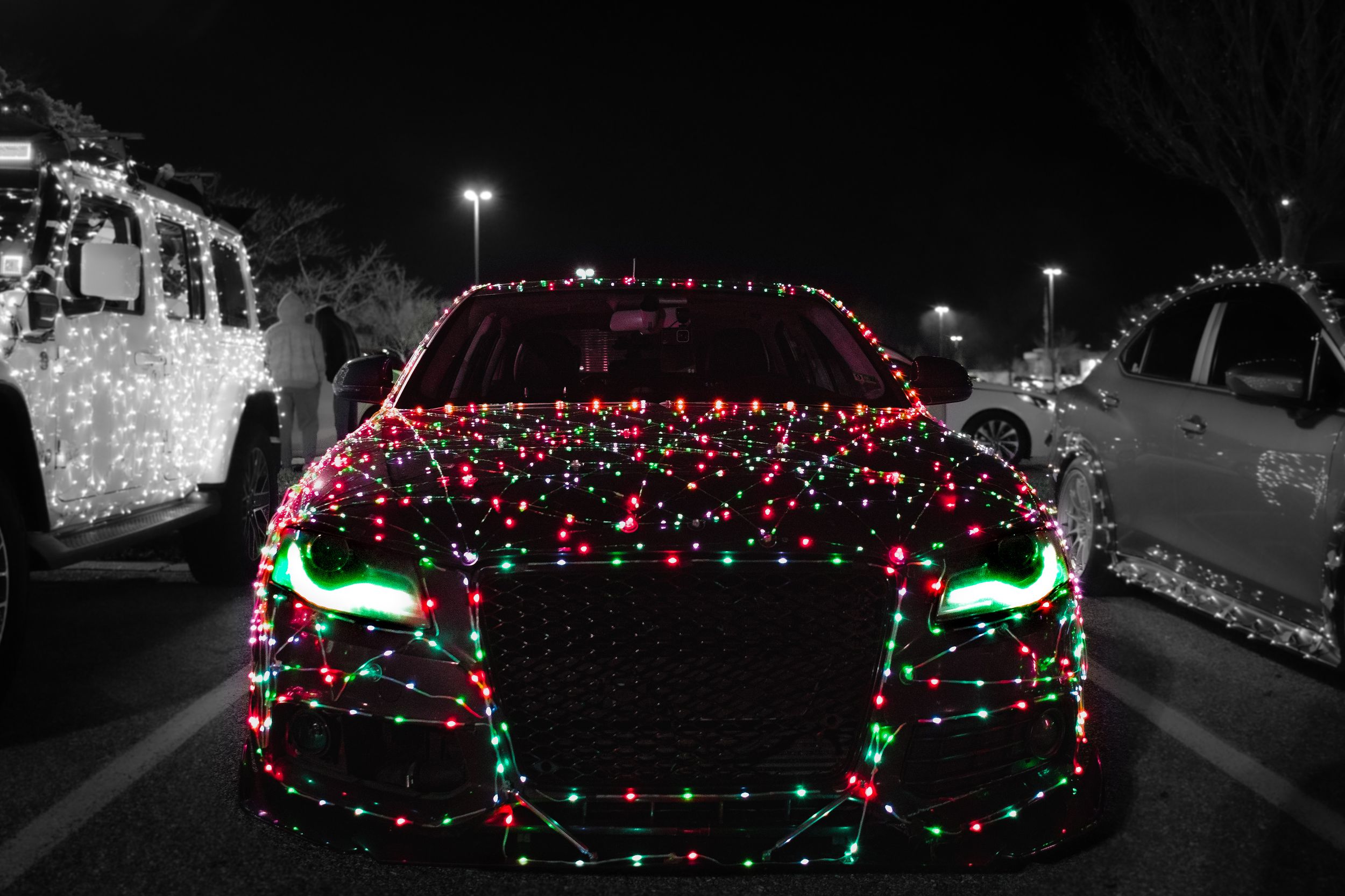 Car covered in red and green Christmas lights glows in dark parking lot at night.