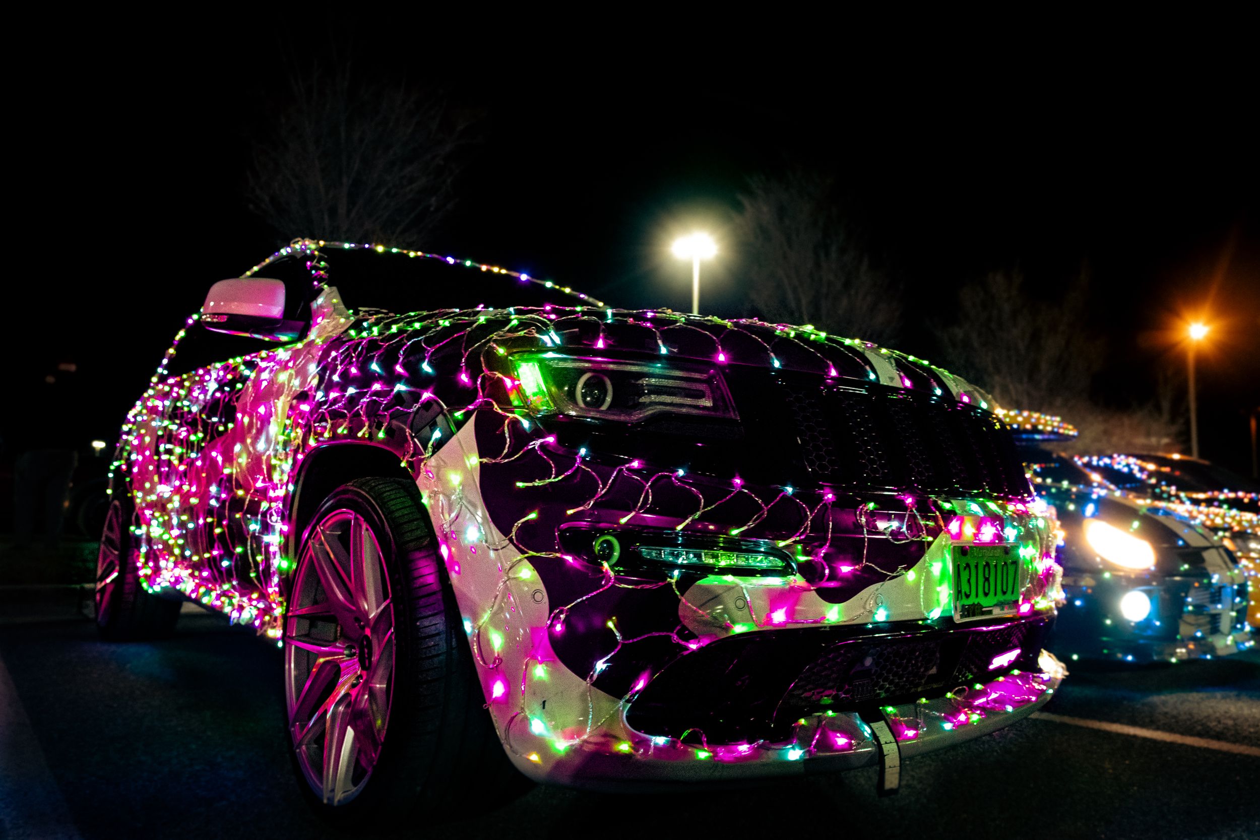 A sports car covered in colorful Christmas lights glowing pink and green at night.