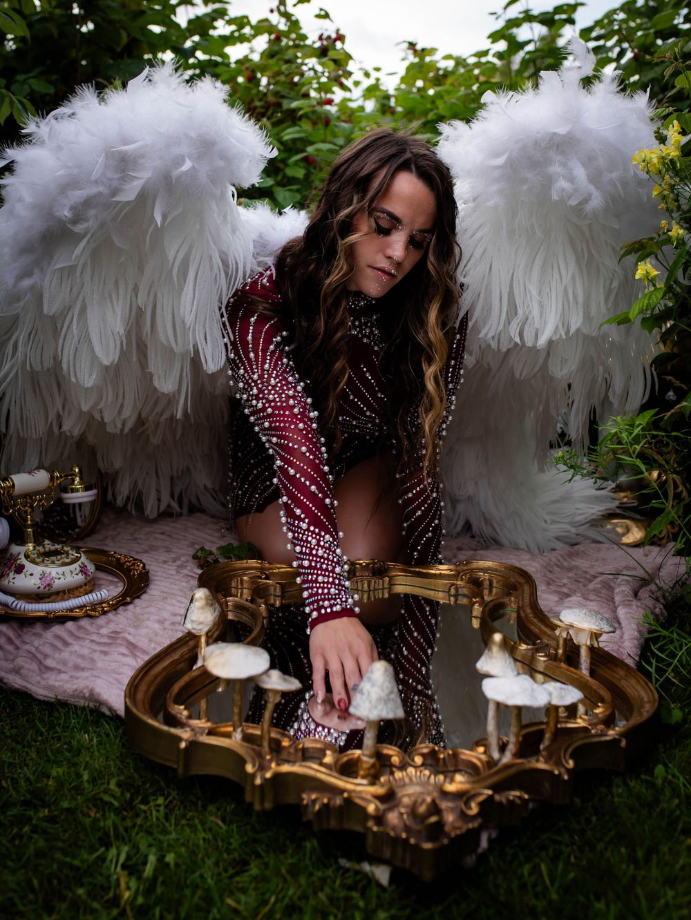 Angel wing photoshoot with model in sequined dress arranging candles on mirrored tray.