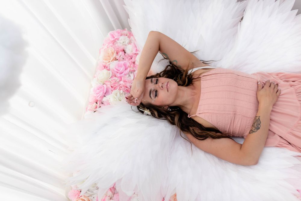 Dreamy portrait with pink dress and feathers against white backdrop.