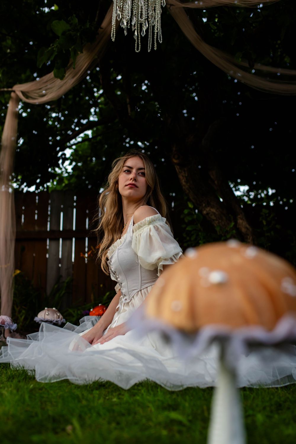 Whimsical garden scene with white dress and decorative mushroom under crystal chandelier.