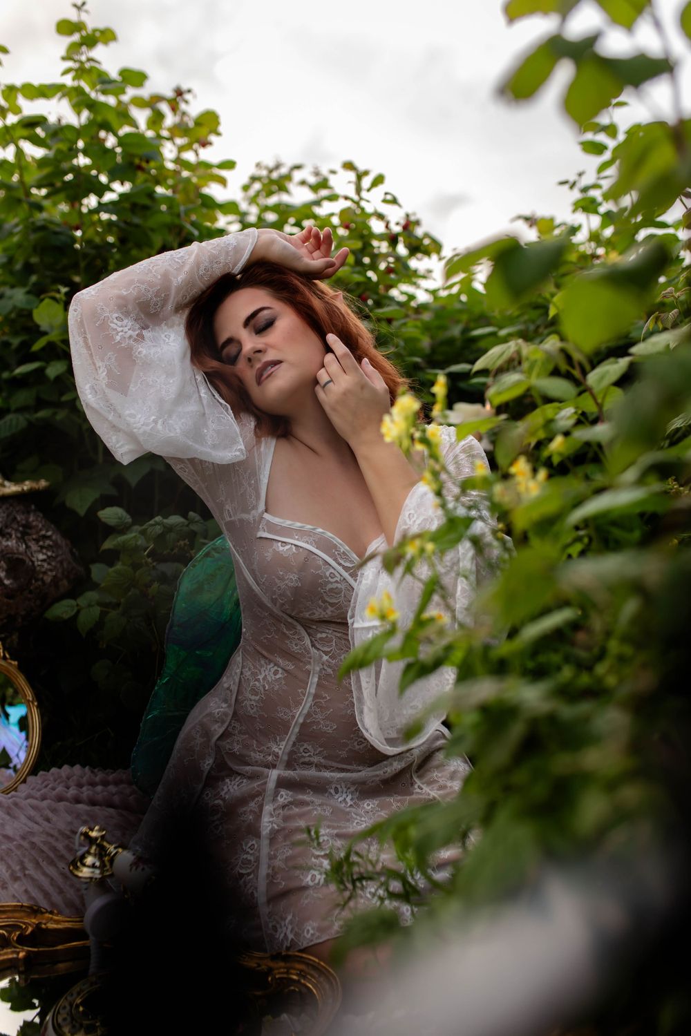 Ethereal garden portrait with flowing white lace dress among green foliage.