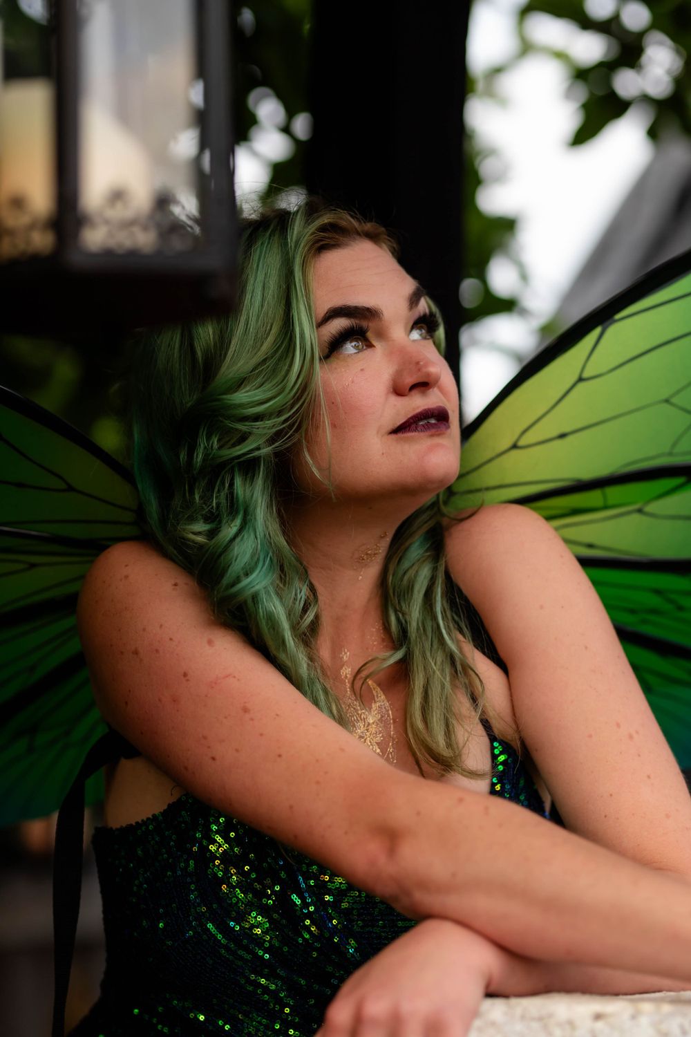 Fantasy fairy portrait with bright green wings and sparkly dress in garden setting.