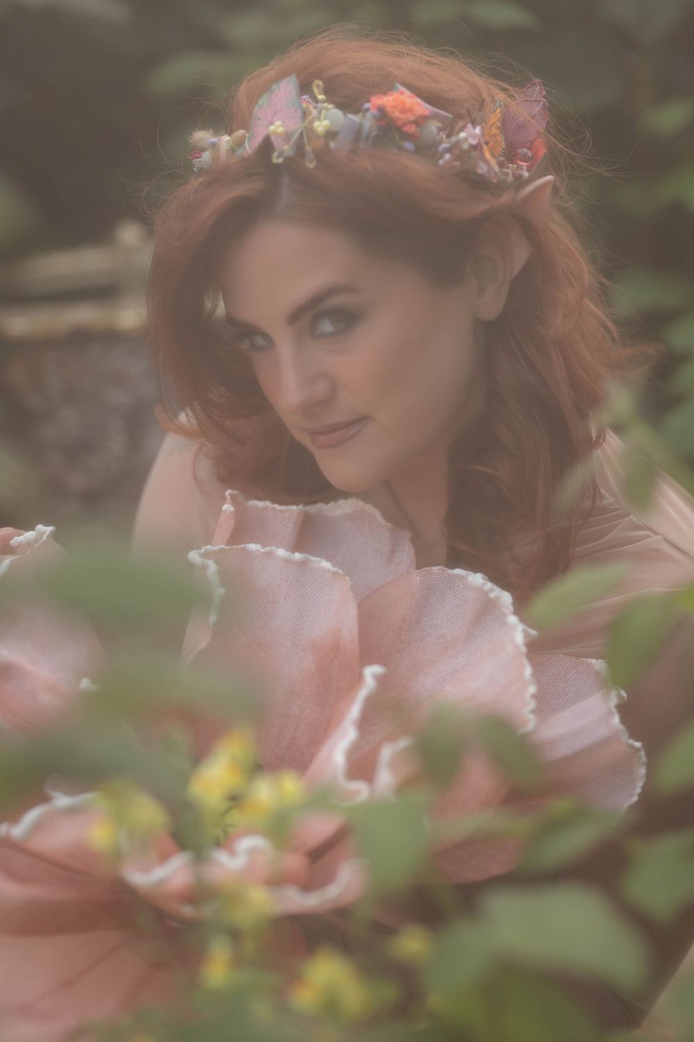 A dreamy portrait with a floral crown and soft pink tones in a romantic garden setting.