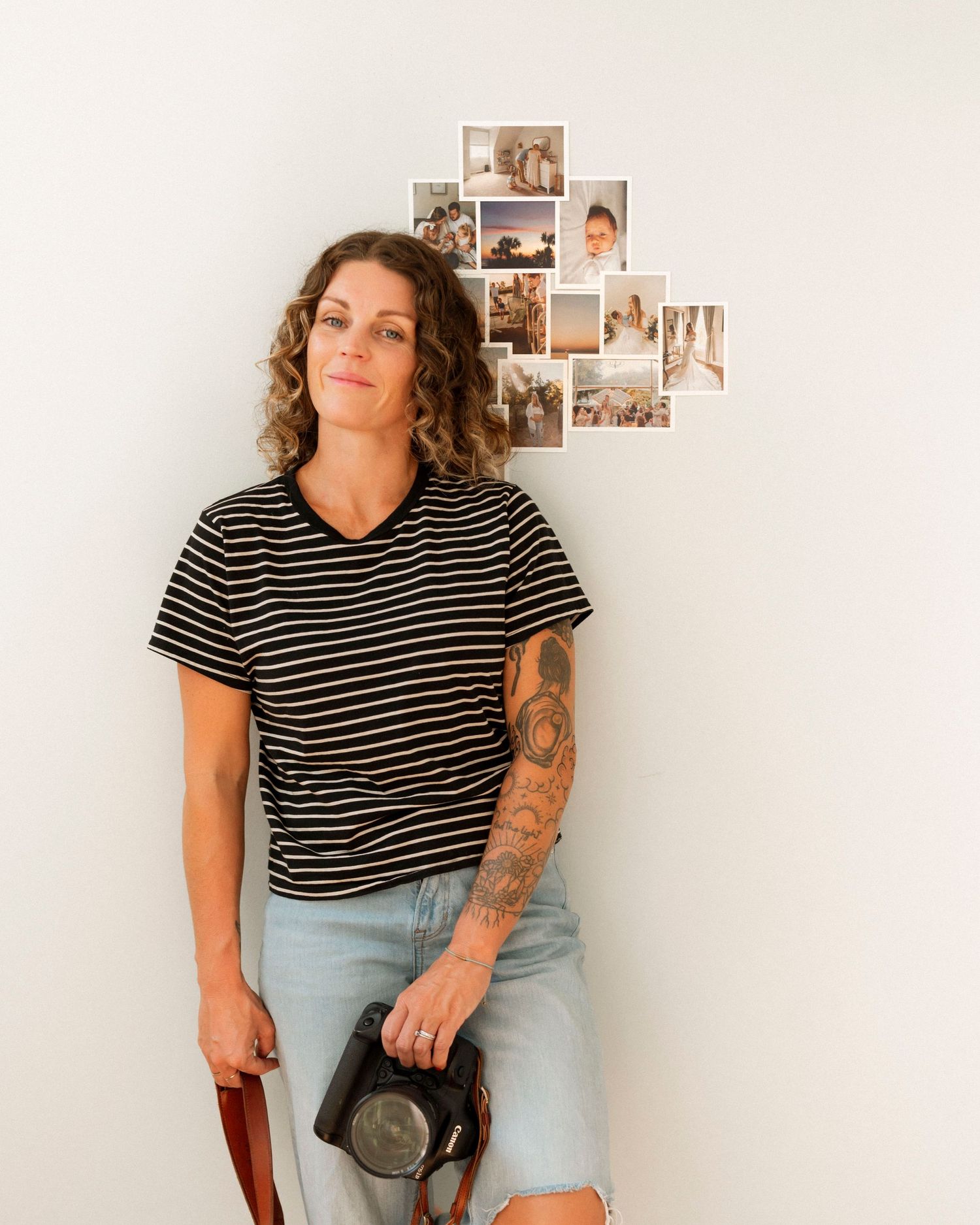 Woman in striped shirt and jeans posing against white wall with photo collage.