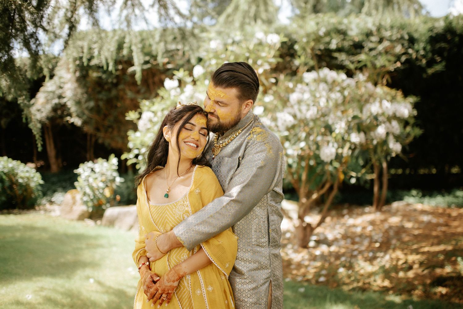A romantic outdoor portrait of a couple embracing in a sunlit garden setting.