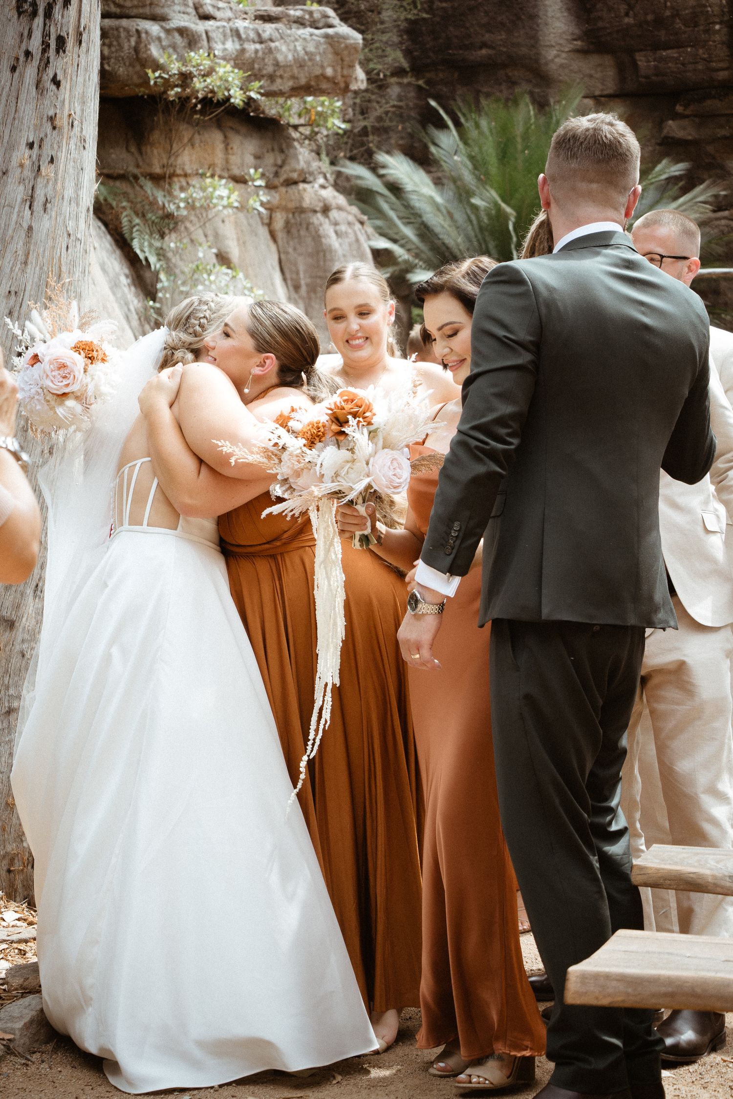 Wedding party members in earth-toned dresses celebrate during an outdoor ceremony.