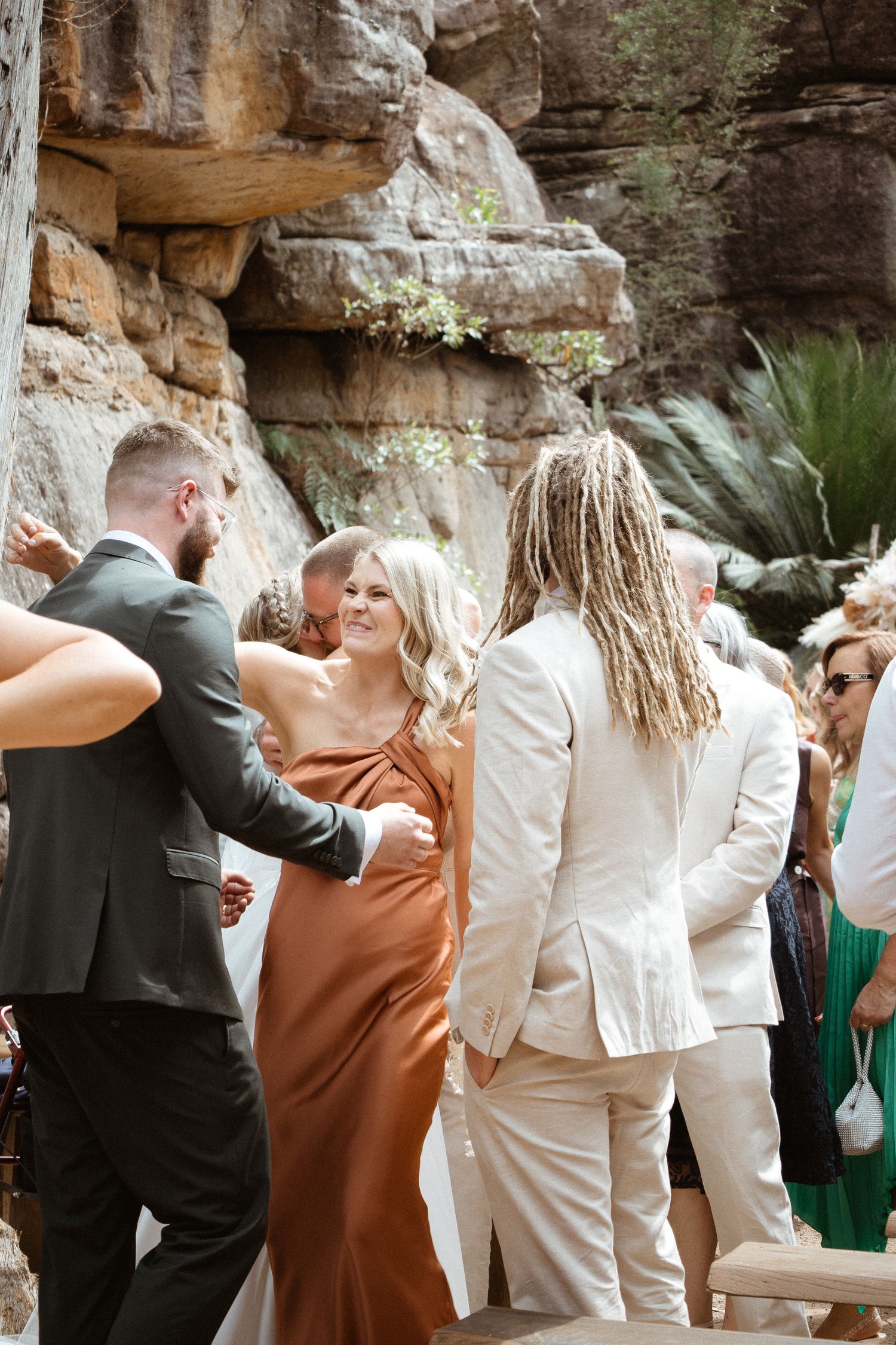 Wedding guests in formal attire socializing during an outdoor celebration near rock formations.