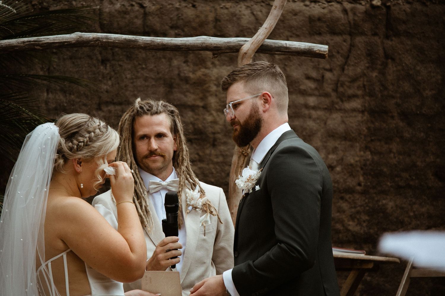 Emotional wedding ceremony moment under rustic arch with stone wall backdrop.