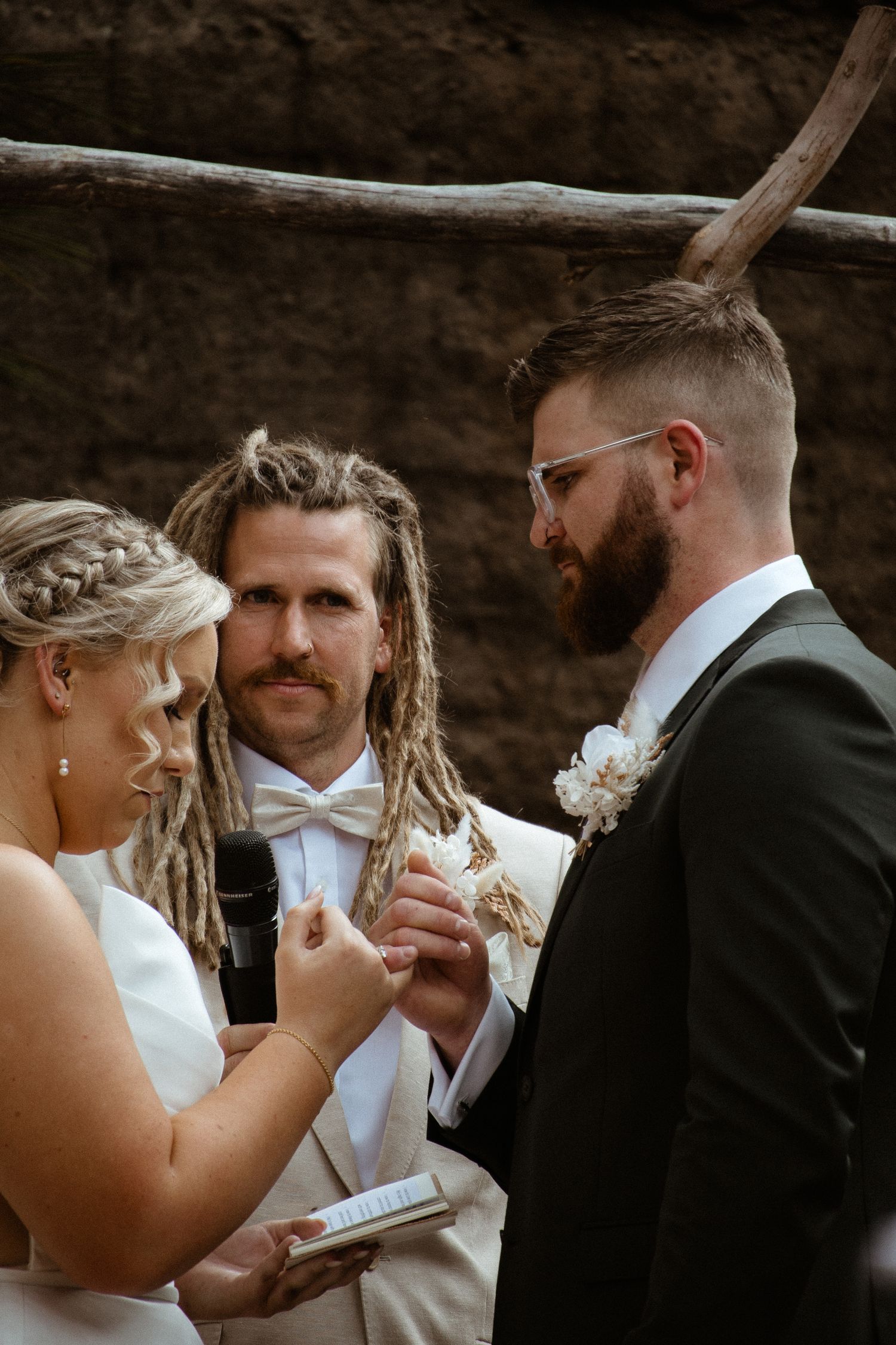 Exchange of wedding vows under wooden arch with pampas grass decor.