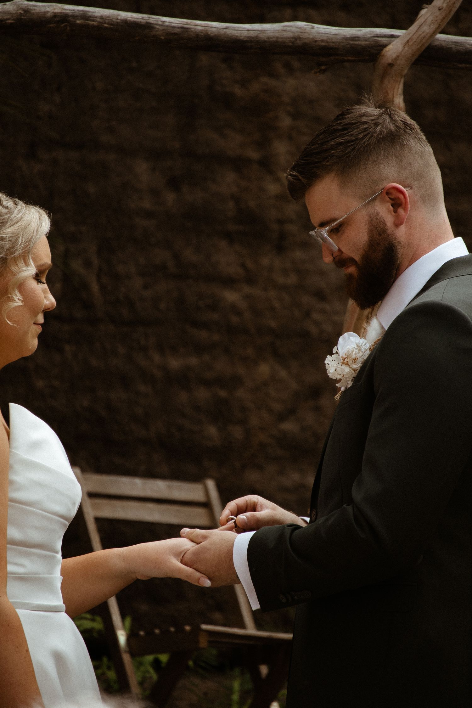 Ring exchange ceremony during intimate outdoor wedding against stone wall backdrop.