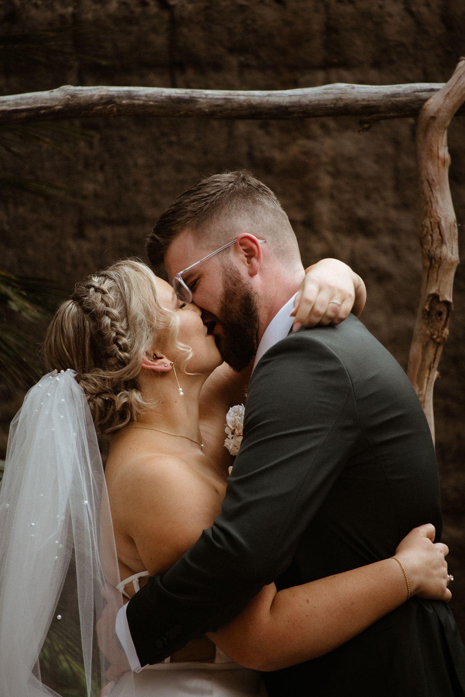 Romantic kiss shared during outdoor wedding ceremony under wooden arch.