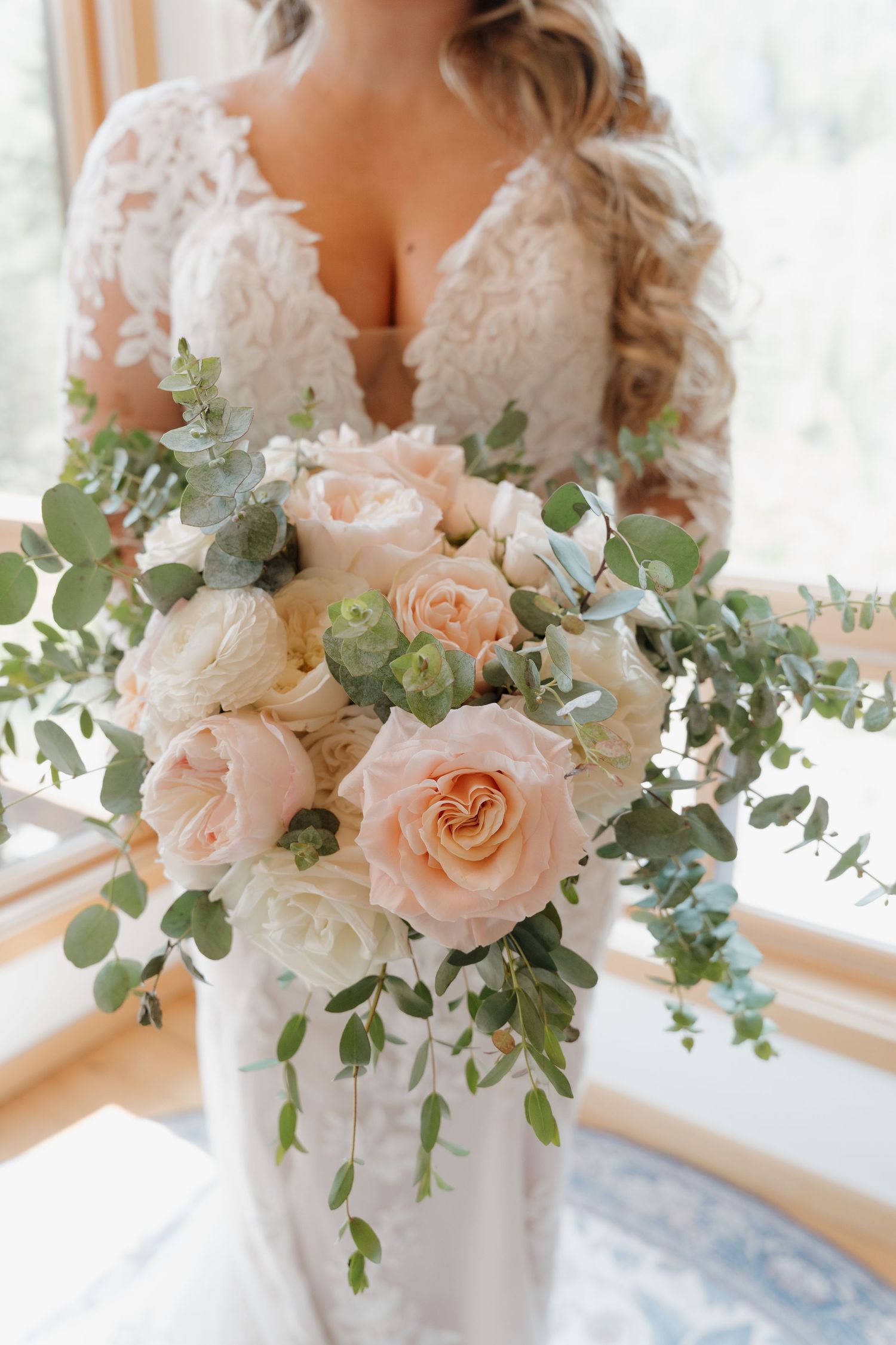 Elegant wedding bouquet with blush pink roses and eucalyptus greenery arranged in a white vase by a window.