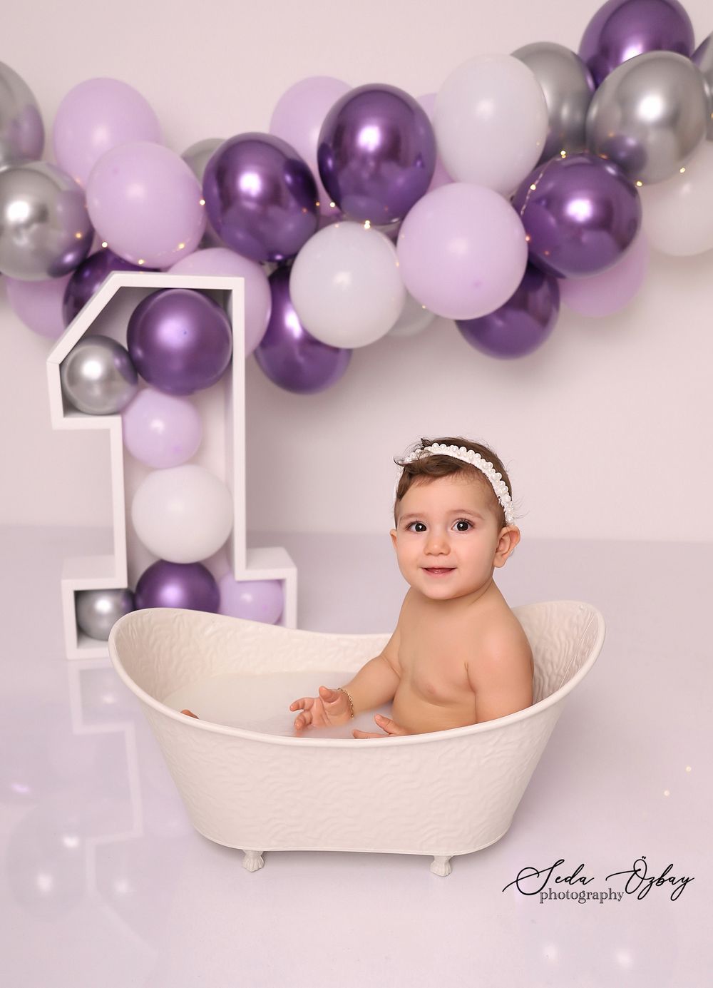 Professional baby photography session with purple and white balloon decorations and a white bathtub prop.