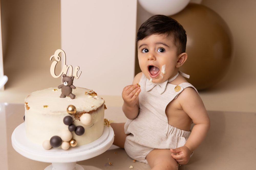 Baby showing excitement next to white birthday cake with gold decorations.
