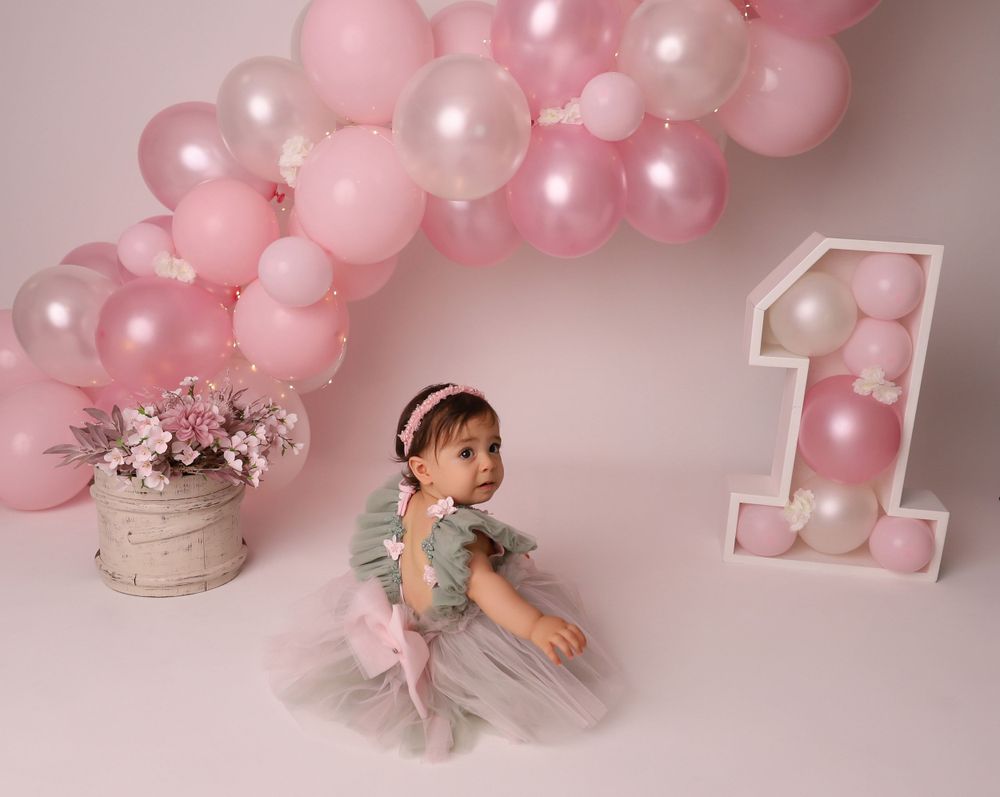 First birthday photography setup with pink balloons and white number one display.
