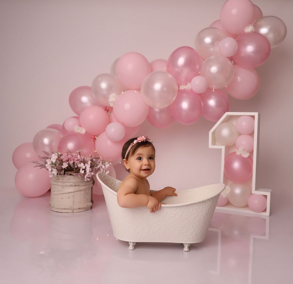 Professional cake smash session with pink balloon arch and white bathtub prop.